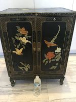 Full front view of black lacquer cabinet showing carved stone motifs and bracket feet