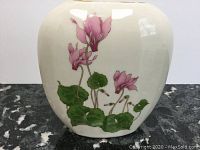 Front view of vase showing detailed cyclamen flowers and leaves on cream ceramic.