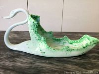 Side view of swan glass dish showing white exterior and green speckled interior with ruffled edges.