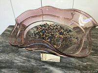 Large Murano glass bowl with wavy edges in pinkish-purple color on a marble surface, showing interior gold and colored flecks.