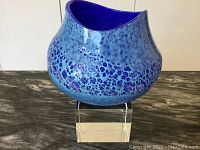 Two-tone blue glass vase on a black marble-like surface and white background. View shows bubble and speckled pattern with asymmetrical opening and deep blue interior color.