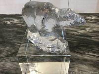 Side view of clear Swedish pressed glass polar bear figurine on a clear glass stand resembling ice.
