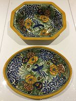 Two hand-painted Talavera ceramic dishes, one octagonal and one oval, featuring floral and bird designs with yellow rims.