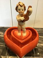 Front view of the Goebel cupid figurine playing violin on heart bowls