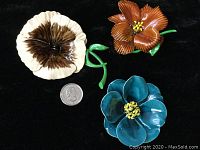 Three enameled flower brooches photographed on a black background alongside a quarter for size reference.