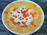 Top close-up view of the round enamel plate with yellow and orange abstract pattern on white background.