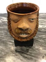 Front view of the signed handmade 1970s pottery face mug showing detailed beard, mustache, closed eyes, and brown glazed interior.