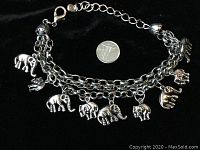Overall view of vintage silver-tone charm bracelet with multiple elephant charms on double chain, showing approximate scale with a coin.