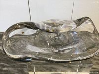 Clear mid-century mouthblown glass bowl or vase shown from top and side view, resting on a clear acrylic stand, on a marble surface.