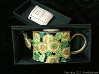 Top view of enamel jug with sunflower design inside original black box showing the overall pattern and colors.