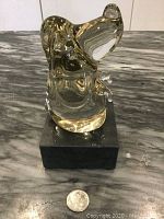 Top front angle of clear blown glass dog figurine on black rectangular stand with coin for size