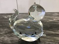 Clear glass cat figurine with curved tail and rounded head, shown on dark marbled surface.