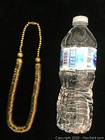 Full view of the vintage metal necklace next to a 500 ml water bottle for size reference, showing the full length and design with tightly stacked bowl-shaped beads.
