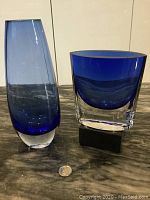 Side view of two Venetian blue glass vases with clear glass bases set on a marble surface with a coin for scale.