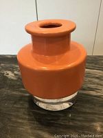 Front view of orange vase showing cylindrical neck, wide body, and clear base on dark surface.