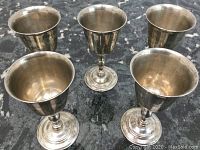 Top and side view of five vintage silver-plated goblets/vases arranged on a dark countertop to show overall shape and size.