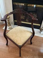 Photo of a wooden corner chair with carved details, cream cushioned seat, placed on wooden floor in front of a fireplace.