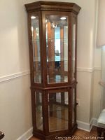 Front view of oak-finished corner curio cabinet showing mirrored back, glass shelves, and recessed dome light