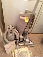 Full overview of upright vacuum, tool caddy with hoses and attachments, manual and vacuum bags on tile floor