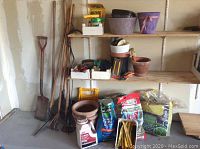 Photo showing multiple wood handled garden tools propped against wall including shovels, rakes, pitchfork and hoes, several bags of fertilizer and soil on floor with various flower pots on shelves and floor