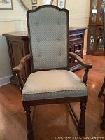 Front view of wooden dining armchair with curved arms, button-tufted back and upholstered seat
