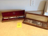 Photo showing the two sets displayed side by side on a countertop: a set of six stainless steel knives with a walnut case labeled Community Stainless and a Gerber carving set in a red-lined walnut case.