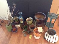 Wide shot of all flower pots, plant stands, and dried pussy willow branches gathered on floor showing their variety and condition.