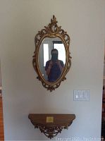 Full view of the oval Victorian mirror and matching wall shelf mounted on a wall, showing the size and style of each piece.