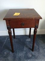 Full view of small wooden side table showing condition, carved details on legs, drawer, and top surface.