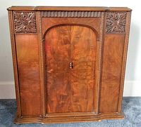 Front view of wood cabinet with sliding doors closed, showing carved floral medallions and central arch design.