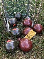 Photo of all bocce balls arranged on grass near vintage green wire milk crate.