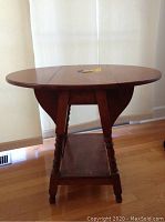Viewing the drop leaf table fully opened, showing oval top and turned legs.