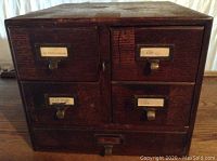 Front view showing 5 drawer fronts with label holders and brass pulls, wood surfaces show wear.