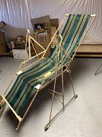 Angled side view of vintage iron swinging lounge chair with green and yellow striped fabric seating and white iron frame.