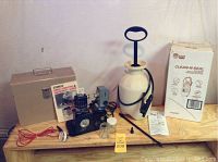 Wide photo of all items on wooden surface including Miller paint sprayer, red hose, Miller manual, Chapin deck sprayer with box and instructions.