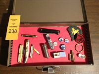 Full lot inside metal case showing knives, pins, patches, ring and coin on red foam
