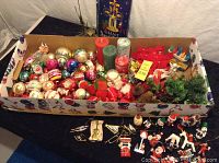 Wide shot of a decorated box filled with assorted vintage Christmas ornaments including glass baubles, candles, and holiday figurines. Angel chimes laid out in front of the box.