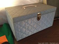 Closed light blue quilted sewing basket with handle and metal lock.