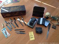 Overall view of the box and assortment of pens, office tools, and accessories on wood floor.