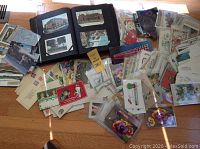 Image showing a large assortment of postcards and envelopes spread on a wooden floor, with a black album open holding some postcards.