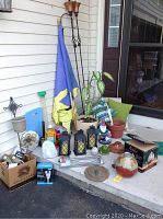 Photo showing assortment of patio garden items including torch lights, cushions, lanterns, garden gnomes, potted plant, and small garden decorations.