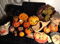 Group photo showing a variety of vintage Halloween decorations and masks arranged on black fabric, including pumpkins, masks, a woven basket, and small items.
