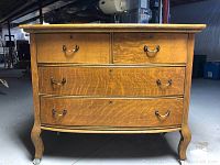Front view of vintage oak chest of drawers showing four drawers and metal handles, chest on curved legs with casters.