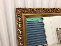 Close-up photo showing the detailed ornate floral and scroll gold carvings on the mirror's frame with a small green label indicating 33 x 44 inches size.