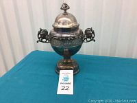 Front view of the silver-plated spooner sugar bowl with lid and ornate handles showing overall shape and decorative elements.