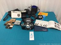 Overview of Nikon FE body, two lenses, filters, flash, cases, manuals arranged on blue surface