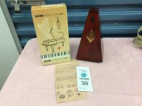 Wittner wooden metronome alongside its original box and instruction sheet, placed on a pink tablecloth.