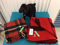 Photo of two wool blankets folded on a blue surface with a black stuffed sheep figurine behind them.
