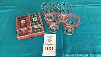 Photo of five unopened Congress playing card decks with tartan patterned boxes and four clear glasses decorated with card suit symbols.