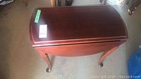 Full view of the wooden folding table showing one drop leaf folded down, cabriole legs, and polished reddish-brown finish.